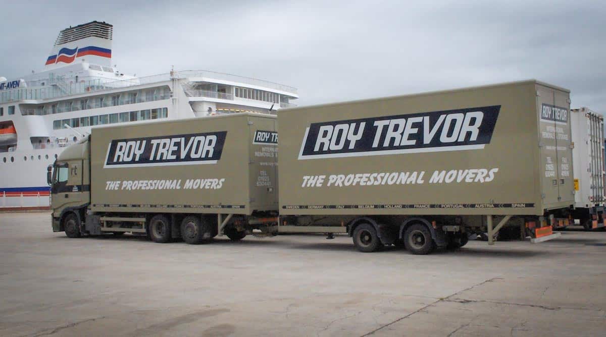 Roy Trevor moving trucks parked beside a large ferry, branded with the slogan “The Professional Movers
